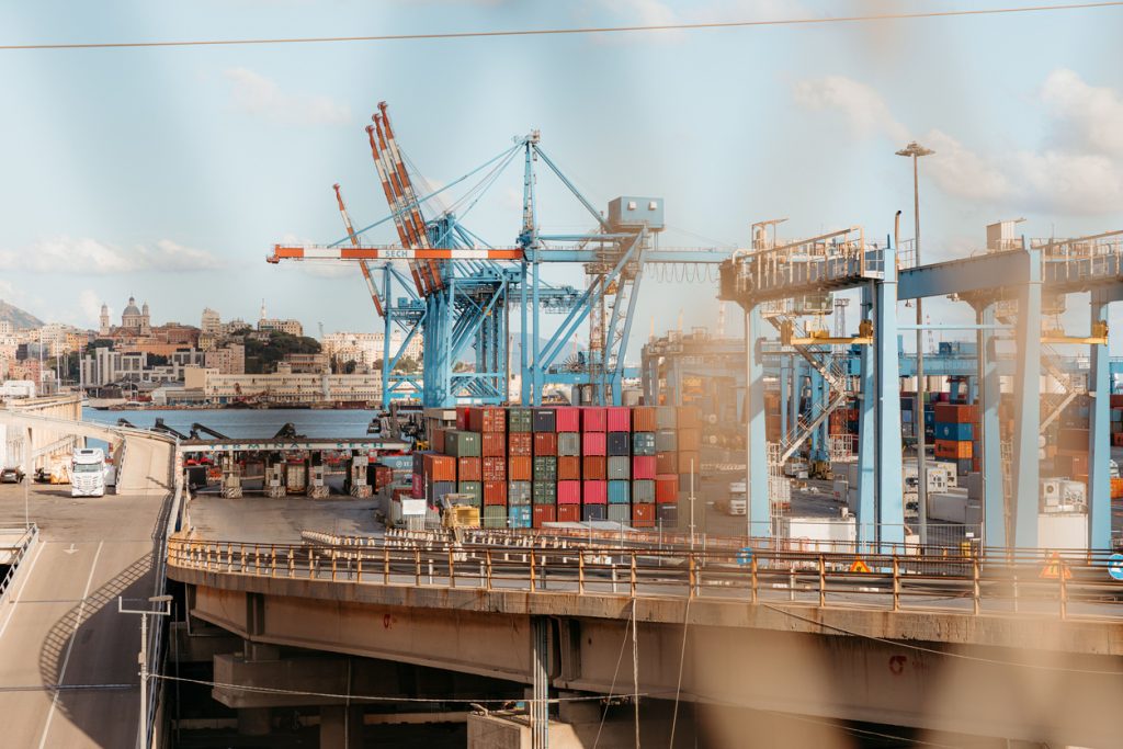 Blaue Verladekräne und hochgestapelte bunte Container dominieren das Bild des industriellen Hafenteils in Genua.