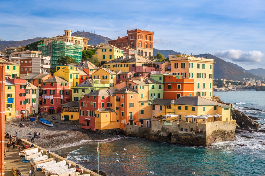 Ein Ensemble aus eng bebauten, bunt gestrichenen Häusern in Genua direkt an der felsigen Küste des Ligurischen Meeres.
