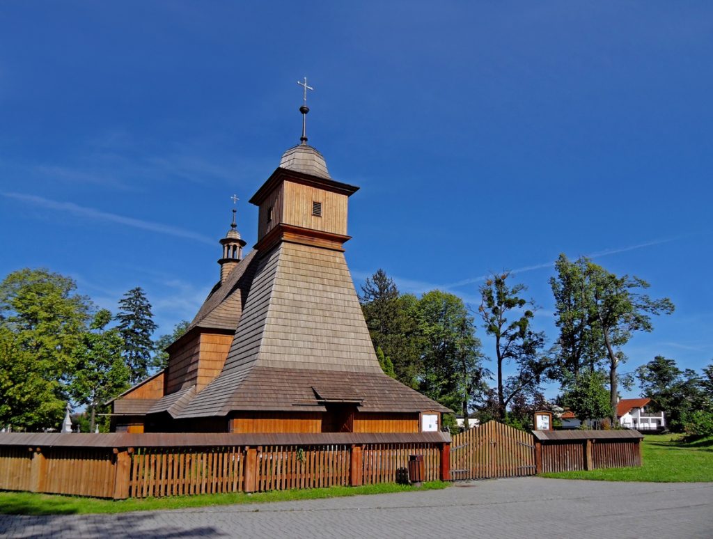 Traditionelle Holzkirche mit schindelgedecktem Dach und kleinem Glockenturm im Grünen.