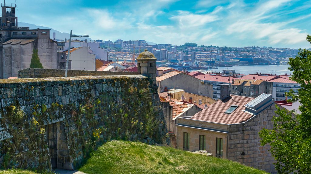 Eine moosbewachsene Steinmauer mit einem kleinen Wachturm bietet einen weiten Ausblick über die roten Dächer der Stadt bis hin zum Hafenbecken.