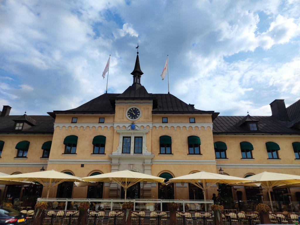 Ein gelbes, historisches Bahnhofsgebäude mit Uhrturm und Restaurant-Terrasse unter einem bewölkten Himmel.