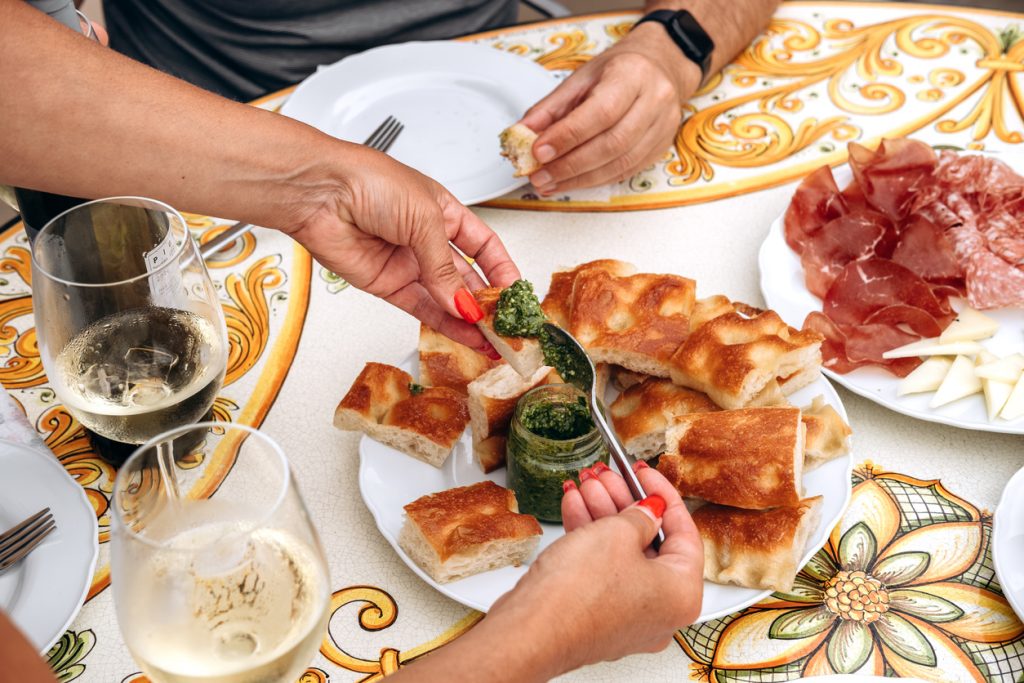 Hände verteilen frisches grünes Pesto auf goldbraunen Focaccia-Stücken in einem Restaurant in Genua.