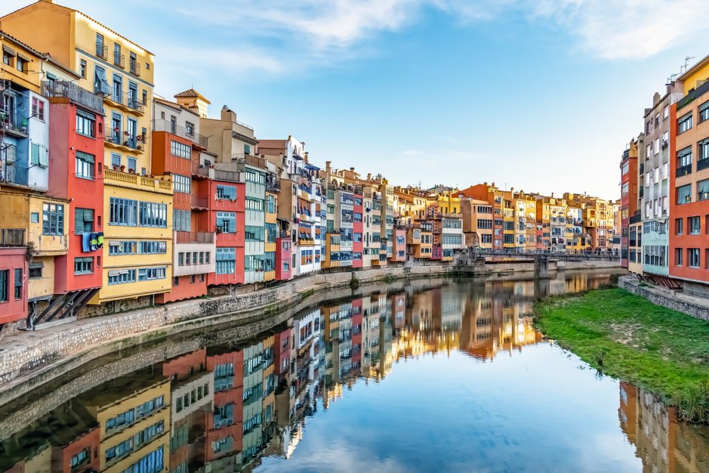 Die ikonischen, bunt gestrichenen Häuser von Girona spiegeln sich im ruhigen Wasser des Flusses Onyar.