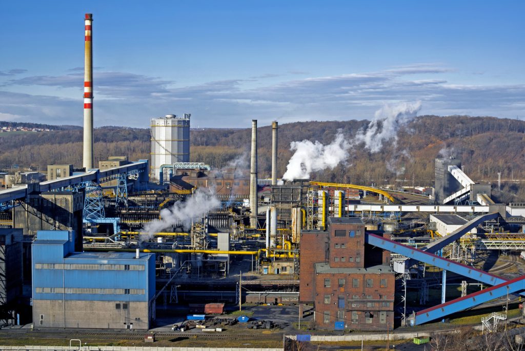 Großes Industrieareal mit Rohren, Förderbändern und Schornsteinen, aus denen Dampf steigt.