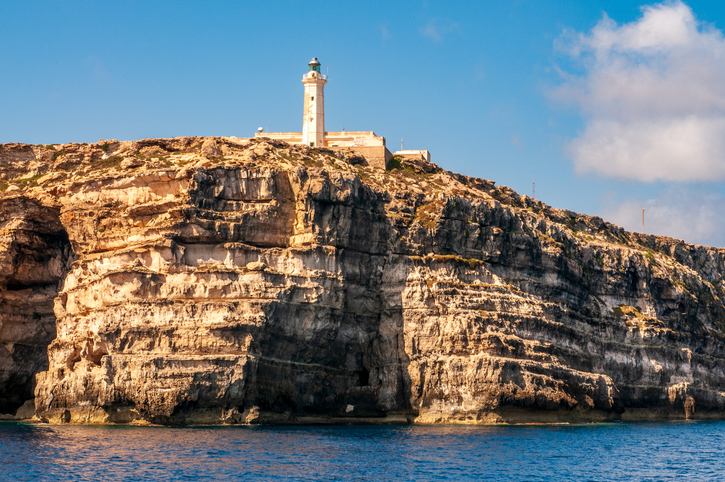 Der weiße Leuchtturm von Capo Grecale thront auf den massiven, hellen Kalksteinklippen über dem dunkelblauen Meer.