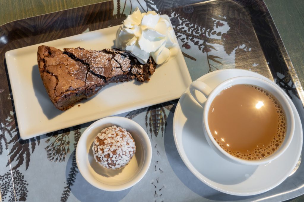 Ein Tablett mit Schokoladenkuchen, Schlagsahne, einer Haferkugel und einer Tasse Milchkaffee steht bereit.