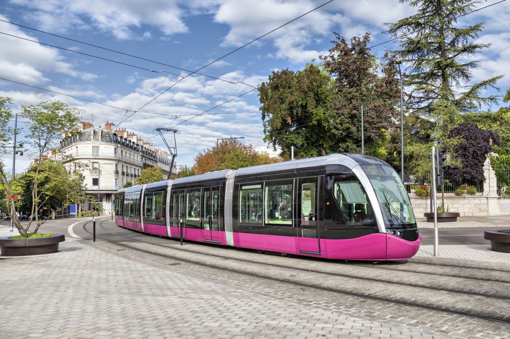 Eine moderne, pink-schwarze Straßenbahn fährt durch die gepflasterten Straßen von Dijon vor einem klassischen Gebäude.