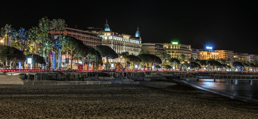 Eine nächtliche Panoramaaufnahme der beleuchteten Hotelpaläste und Palmen entlang der Bucht von Cannes.
