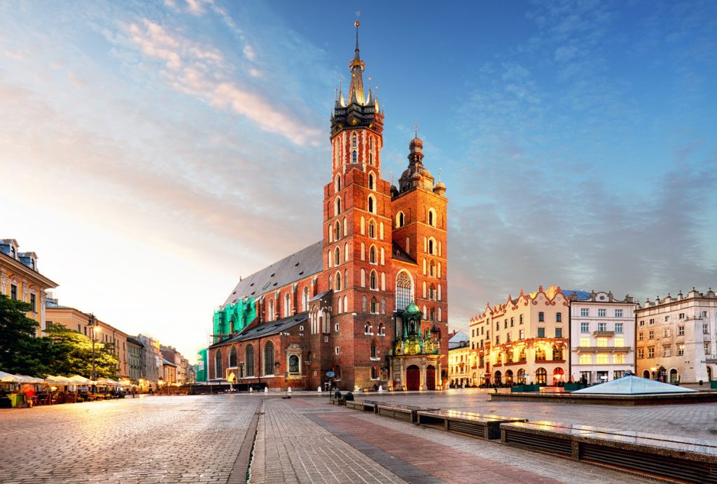 Die backsteingotische Marienkirche in Krakau erstrahlt im warmen Licht der untergehenden Sonne auf dem fast leeren Marktplatz.
