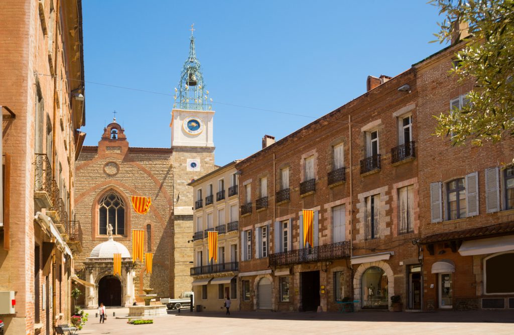 Straße mit Kirche, Uhrturm und Fahnen in der Altstadt von Perpignan.