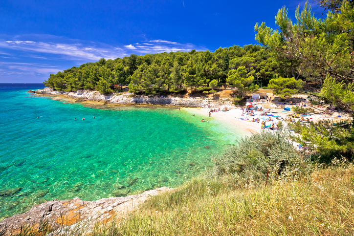 Eine idyllische Badebucht nahe Pula mit türkisblauem Wasser, weißem Kieselstrand und dichten Pinienwäldern.