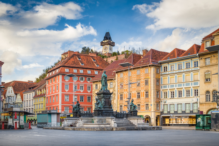 Ein weiter Platz mit einem großen Monumentalbrunnen im Vordergrund und dem Schloßberg im Hintergrund.