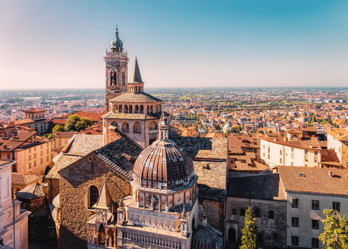 Mehrere Kirchenkuppeln und ein hoher Glockenturm ragen über die dicht bebaute Altstadt von Bergamo hinaus.