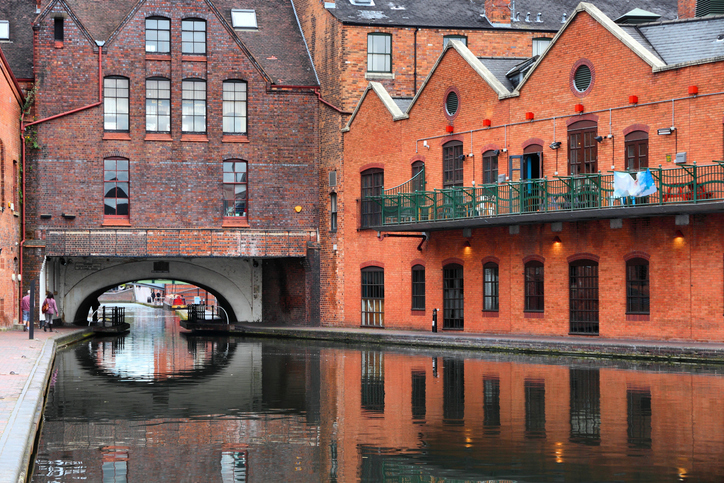 Rote Backsteingebäude stehen dicht an einem ruhigen Kanal, der sich unter einem Gebäude hindurchzieht.