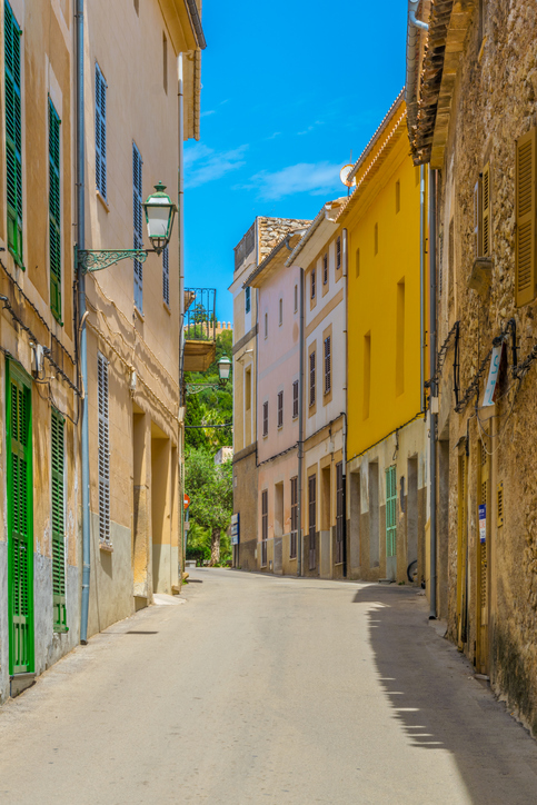 Eine schmale Straße mit hellen Häuserfassaden und grünen Fensterläden führt durch die Altstadt.