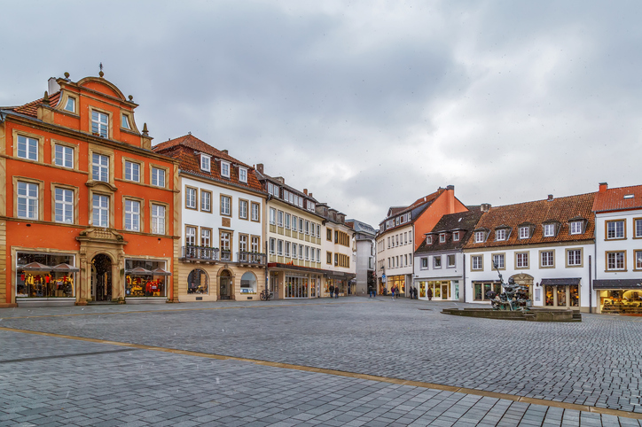 Großer gepflasterter Platz mit bunten Bürgerhäusern und einem Brunnen unter bewölktem Himmel.