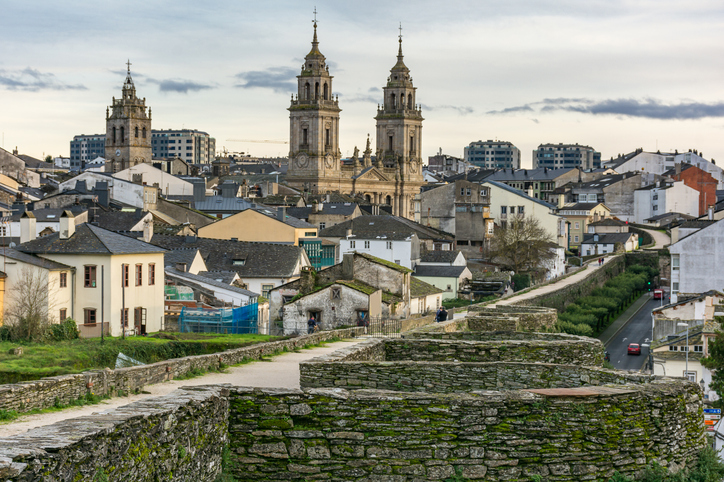 Blick von der römischen Stadtmauer über die Dächer der Altstadt von Lugo hin zur Kathedrale unter einem bewölkten Abendhimmel.