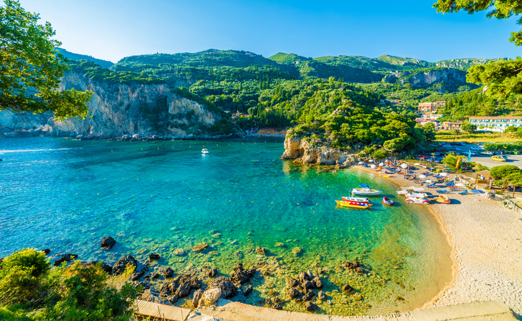 Eine hufeisenförmige Bucht mit türkisblauem Wasser, einem hellen Sandstrand und bunten Booten vor bewaldeten Bergen.