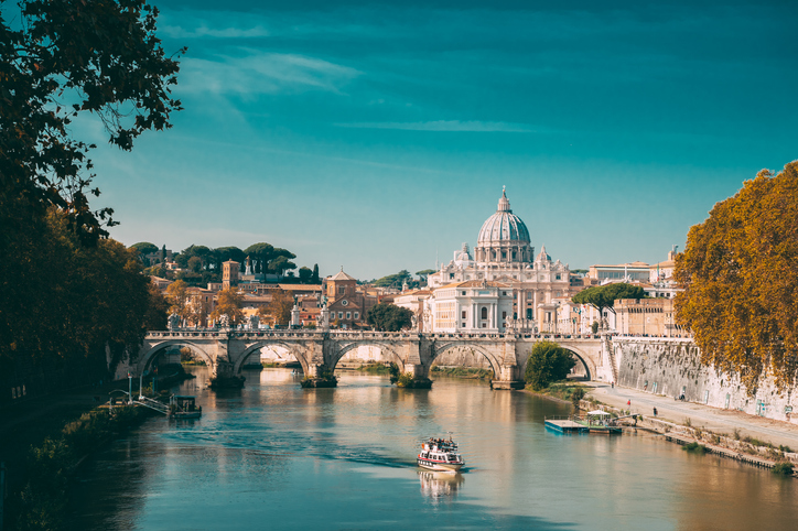 Blick vom Tiber auf die Engelsbrücke mit ihren Engelsstatuen, im Hintergrund die markante Kuppel des Petersdoms.