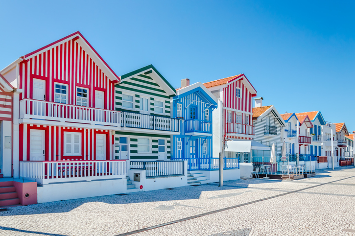 Leuchtend rot, grün und blau gestreifte Strandhäuser mit Balkonen an einer Promenade.