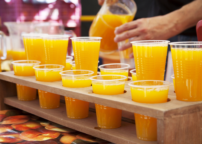 Zahlreiche Plastikbecher gefüllt mit leuchtend gelbem Orangensaft auf einem Holzgestell.
