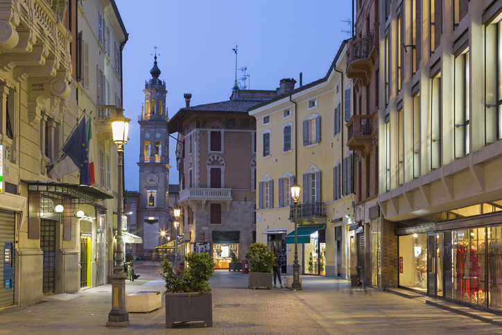 Eine ruhige Einkaufsstraße in Parma führt bei Abendlicht auf einen historischen Turm zu.