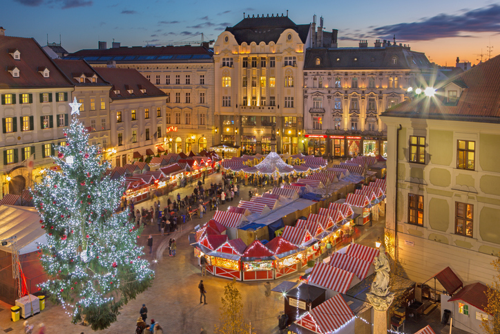 Ein großer Weihnachtsbaum und viele rot weiß gestreifte Marktstände füllen einen festlich beleuchteten Platz.