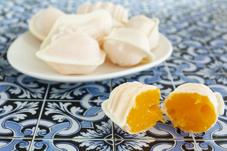 Mehrere weiße, weiche Gebäckstücke auf einem Teller, eines davon aufgeschnitten mit leuchtend gelber Füllung, auf blau-weißen Fliesen.