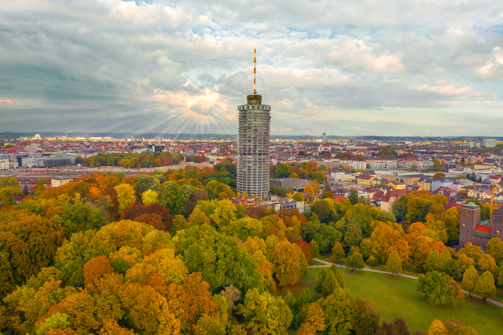 Luftaufnahme des Augsburger Hotelturms umgeben von herbstlich bunten Bäumen im Wittelsbacher Park.