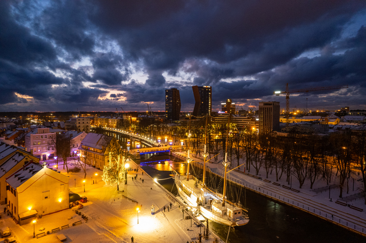 Ein beleuchteter Kanal mit Segelschiff und verschneiten Ufern liegt unter dunklen Wolken.