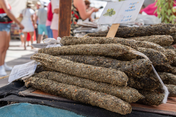 Stapel von Fuet-Salami mit verschiedenen Kräuterkrusten auf einem Wochenmarkt auf Mallorca.