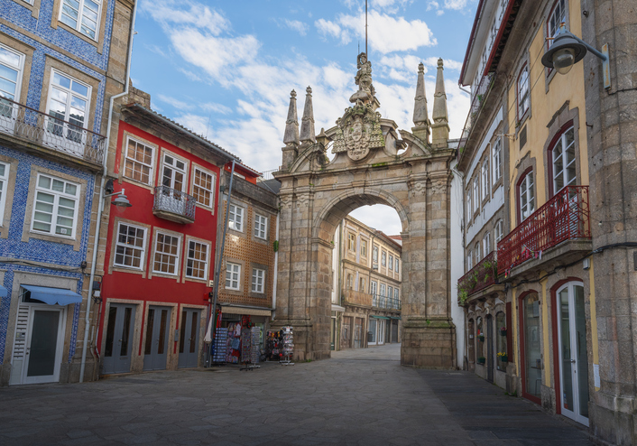 Ein mächtiges steinernes Torhaus am Ende einer Straße mit farbenfrohen Häusern in Braga.
