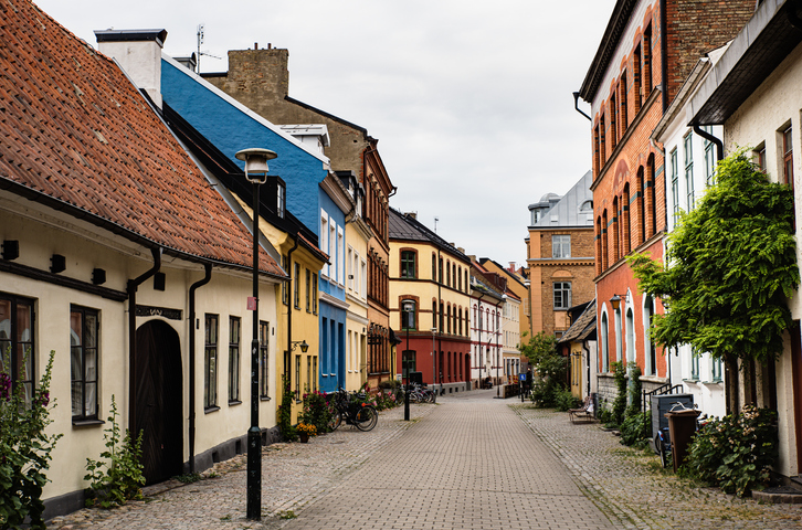 Eine schmale Straße gesäumt von farbenfrohen Häusern in Gelb, Orange und Weiß unter einem bewölkten Himmel.