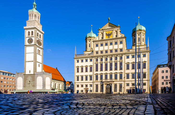 Das Renaissance-Rathaus von Augsburg neben dem Perlachturm unter strahlend blauem Himmel.