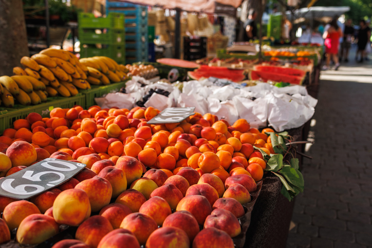 Ein Marktstand in Alcudia mit einer Fülle an frischen Pfirsichen, Aprikosen und Bananen unter einem Sonnensegel.