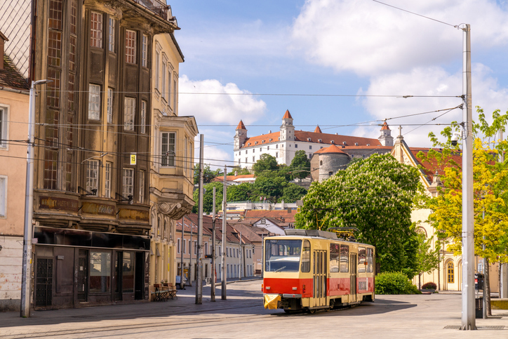 Eine rot cremefarbene Straßenbahn fährt durch eine Straße, im Hintergrund liegt die Burg auf einem Hügel.