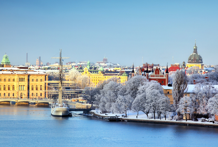 Ein weißer Segler liegt im Hafen vor den schneebedeckten Bäumen und historischen Gebäuden der Stockholmer Altstadt.