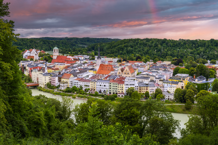 Panoramaaufnahme von Rosenheim mit bunten Häuserreihen am Flussufer unter einem dramatischen Abendhimmel.