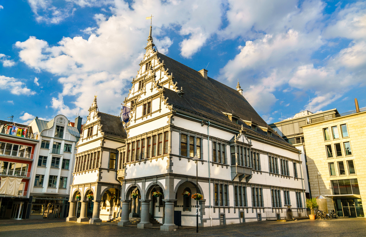 Ein weißes, verziertes Barockgebäude an einem Platz unter blauem Himmel mit Wolken.