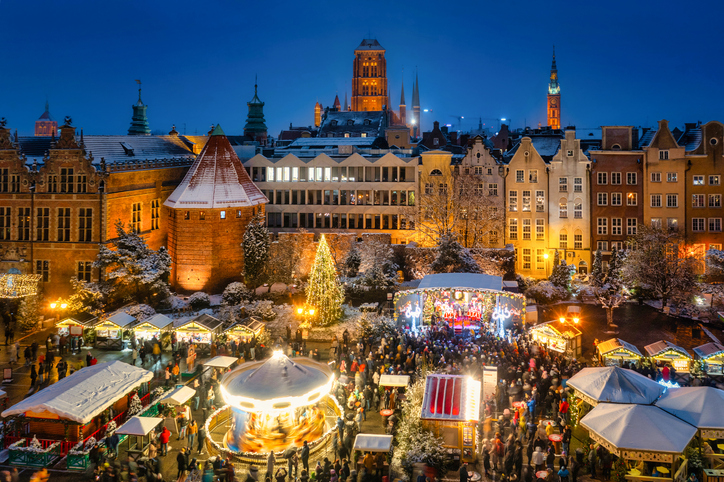 Ein festlich beleuchteter Weihnachtsmarkt mit Karussell und vielen Ständen füllt einen Platz am Abend.
