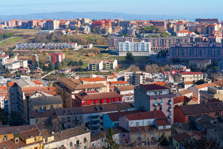 Weiter Blick über rote Dächer, moderne und traditionelle Häuser in der hügeligen Stadtlandschaft.