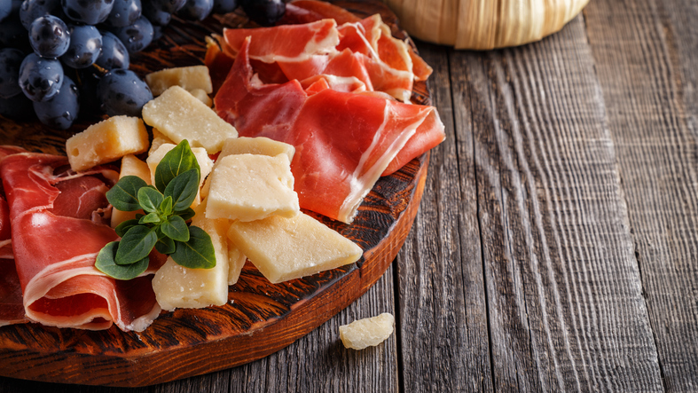 Dünner Schinken und Käsestücke liegen auf einem rustikalen Holzbrett.