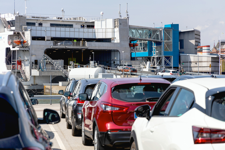 Wartende Autos in einer Schlange vor der großen Auffahrrampe einer weißen Ostseefähre im Hafen.