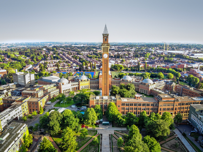 Eine Luftaufnahme zeigt den Campus der University of Birmingham mit dem markanten Uhrturm inmitten vieler Gebäude und Grünflächen.
