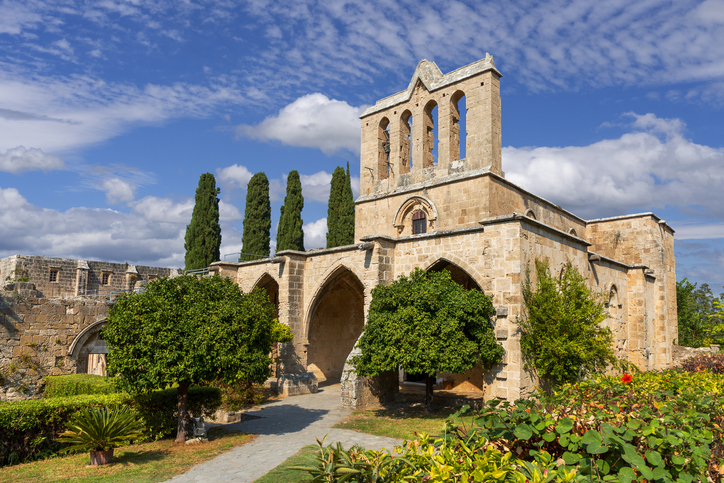 Ein altes Kloster mit Bögen, Bäumen und Garten steht unter blauem Himmel.