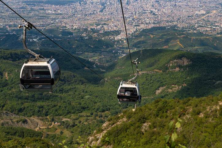 Gondeln der Dajti Ekspres Seilbahn schweben über bewaldeten Hügeln mit Blick auf Tirana.
