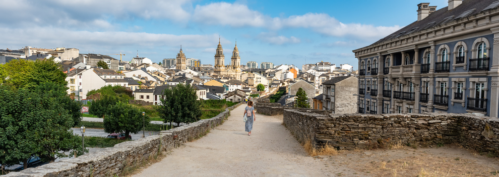 Eine weite Panoramaaufnahme des Spazierwegs auf der römischen Stadtmauer von Lugo mit Blick auf die Stadt und die Kathedrale in der Ferne.