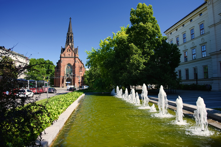 Ein langes Wasserbecken liegt vor einer Kirche und hellen Gebäuden.