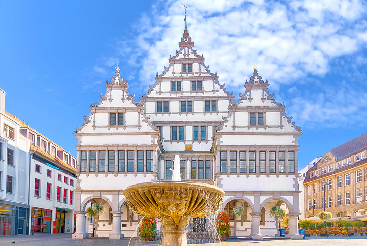 Frontansicht des historischen Rathauses von Paderborn mit drei Giebeln und einem Brunnen davor.