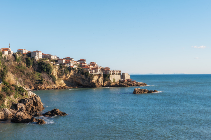 Häuser auf einer felsigen Küste blicken über das ruhige blaue Meer.